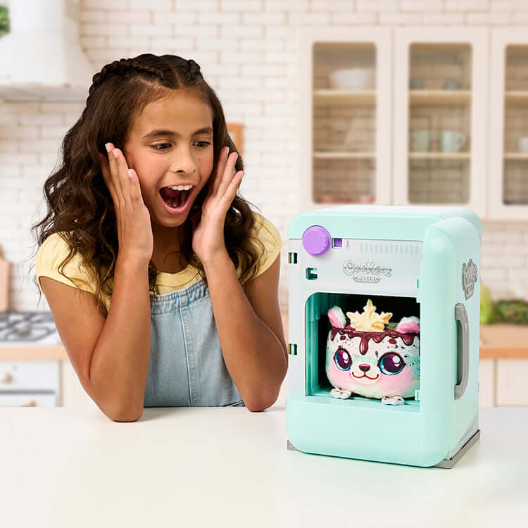 Child excitedly discovering a surprise plush toy inside the Cookeez Makery S2 Freezy Cakez Playset in a kitchen setting.